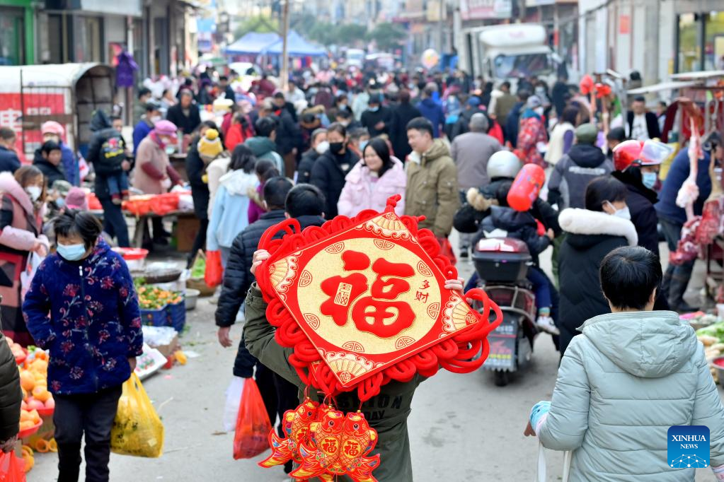 A villager carrying a festive decoration on the back is pictured in a market in Jingzi Town of Shuangfeng County, central China's Hunan Province, Jan. 18, 2023. This year's Spring Festival, or the Chinese New Year, falls on Jan. 22. (Photo by Li Jianxin/Xinhua)